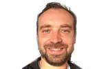 Portraitfoto eines Mannes mit Bart und einem freundlichen Lächeln.
