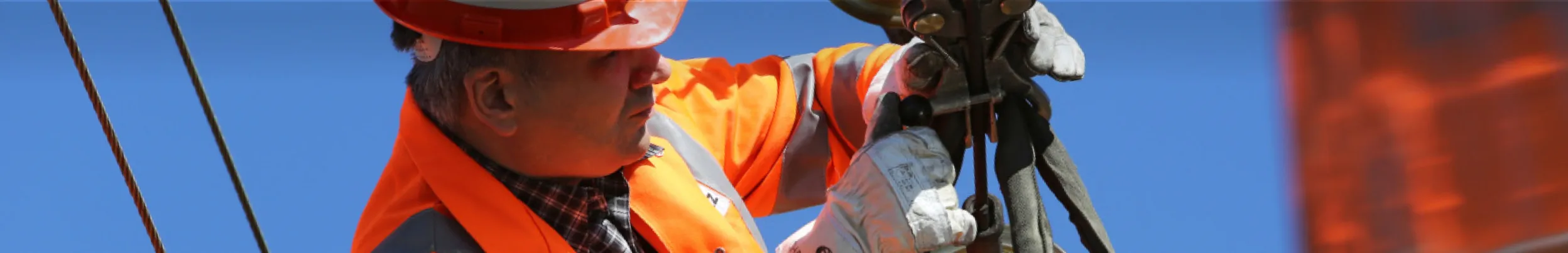 Arbeiter in oranger Schutzkleidung auf einer Bahnstrecke mit Werkzeug im Einsatz.