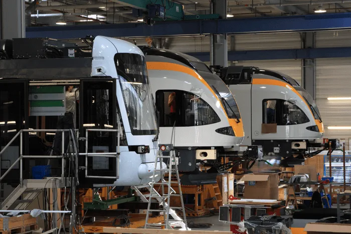 Montagehalle mit modernen Zügen und Technikern bei der Arbeit.