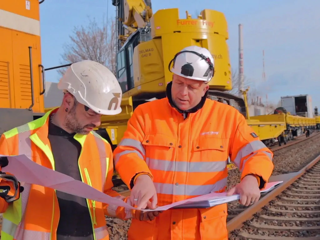 Mitarbeiter in Warnwesten arbeiten an einer Oberleitung auf einer Bahnstrecke.
