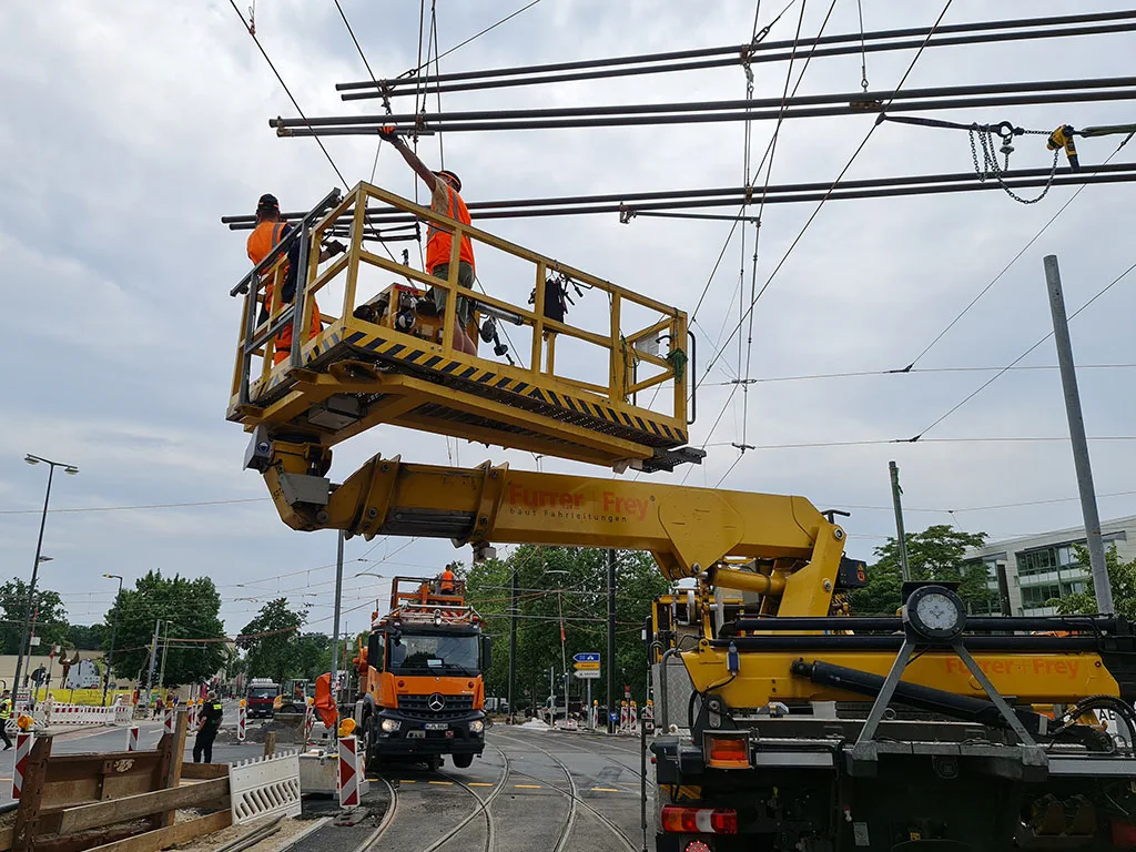 Bauarbeiten an Oberleitungen mit mehreren Spezialfahrzeugen und Arbeitern.