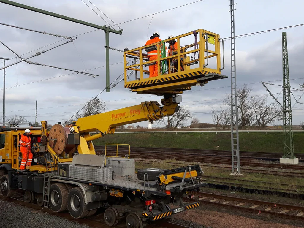 Arbeiter in Warnwesten arbeiten an einer Oberleitung mit einem Spezialfahrzeug.
