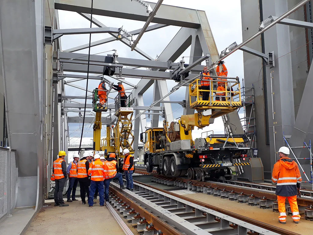 Fahrzeug hebt Arbeiter zu Oberleitungen während Bauarbeiten auf einer Bahnstrecke.